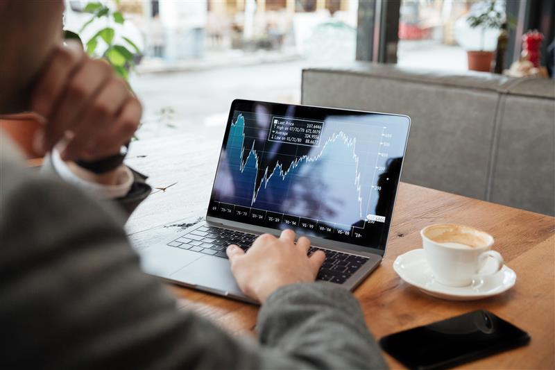 A trader sitting at a table in a cafe, analyzing financial indicators on a device.